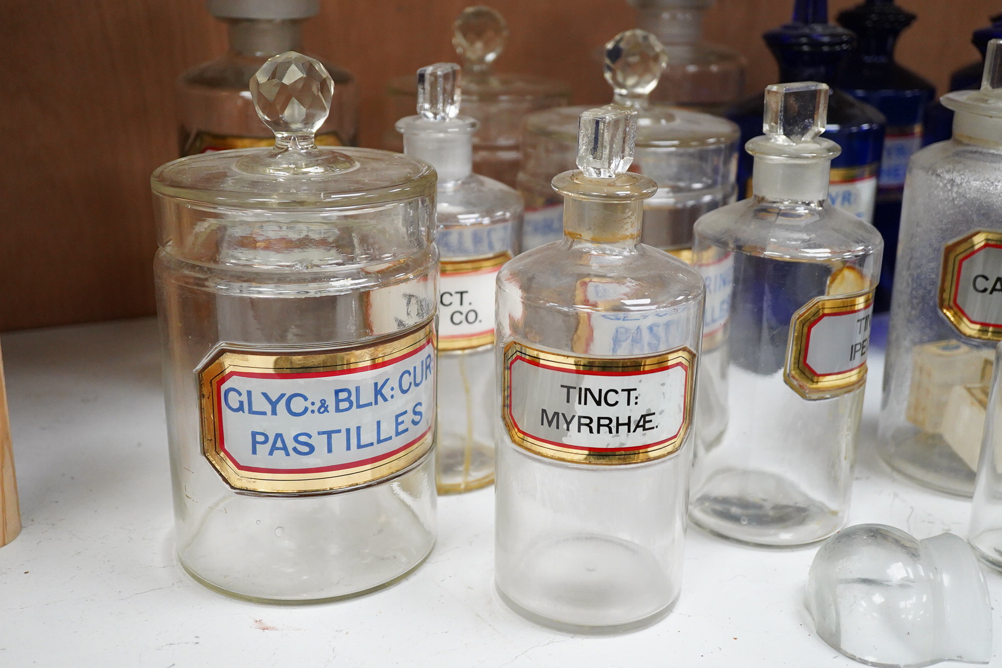 Seventeen 19th/early 20th century glass apothecary jars with gilt rimmed labels; six blue glass, ten clear glass and a green glass example, labels including; Syr: Zingib:, Chloroform, Syr: Rhei:, Camphora, etc. tallest 2